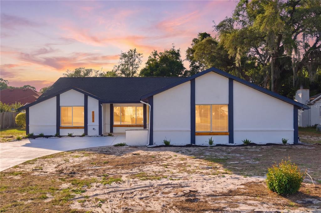 A single-story house with white stucco walls, dark blue trim, and a concrete driveway — 1215 WATERFALL DRIVE, SPRING HILL, FL