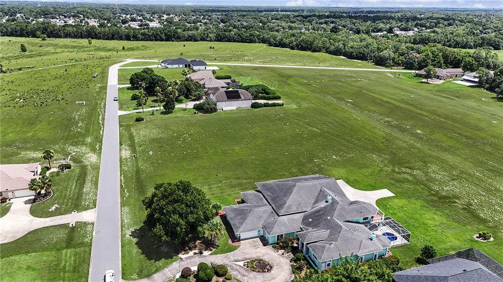 An aerial view shows a residential airpark with houses lining a grassy runway and road — 8491 SE 72ND AVENUE, OCALA, FL