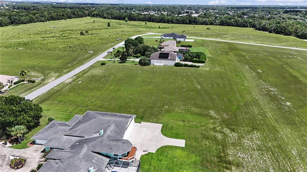 An aerial view shows a large, grassy vacant lot adjacent to a light green house — 8491 SE 72ND AVENUE, OCALA, FL
