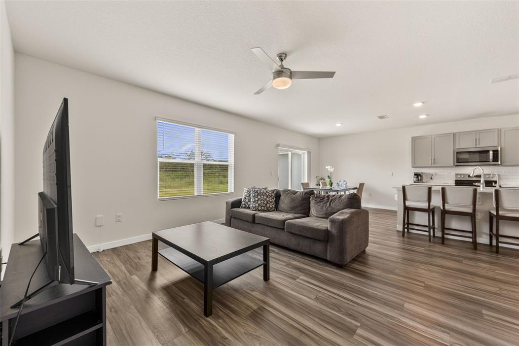 An open-concept living room and kitchen featuring wood-look flooring, a grey sofa, and a ceiling fan — 416 TALISI LOOP, ST CLOUD, FL