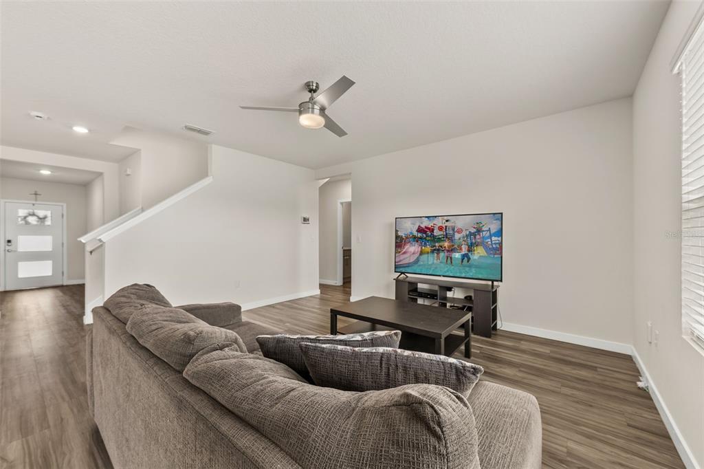 A living room features gray wood-look flooring, a gray sofa, and a television on a stand — 416 TALISI LOOP, ST CLOUD, FL