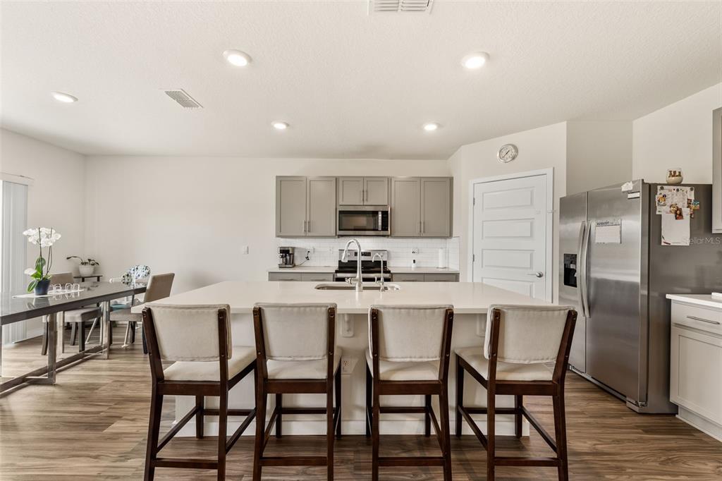 A kitchen features a large island with four bar stools, grey cabinets, and stainless steel appliances — 416 TALISI LOOP, ST CLOUD, FL