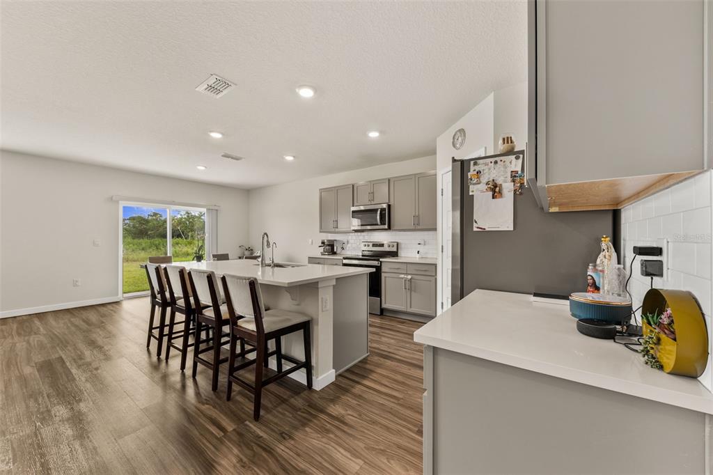 A kitchen with a large island, gray cabinetry, and wood-look flooring opens to a living area — 416 TALISI LOOP, ST CLOUD, FL