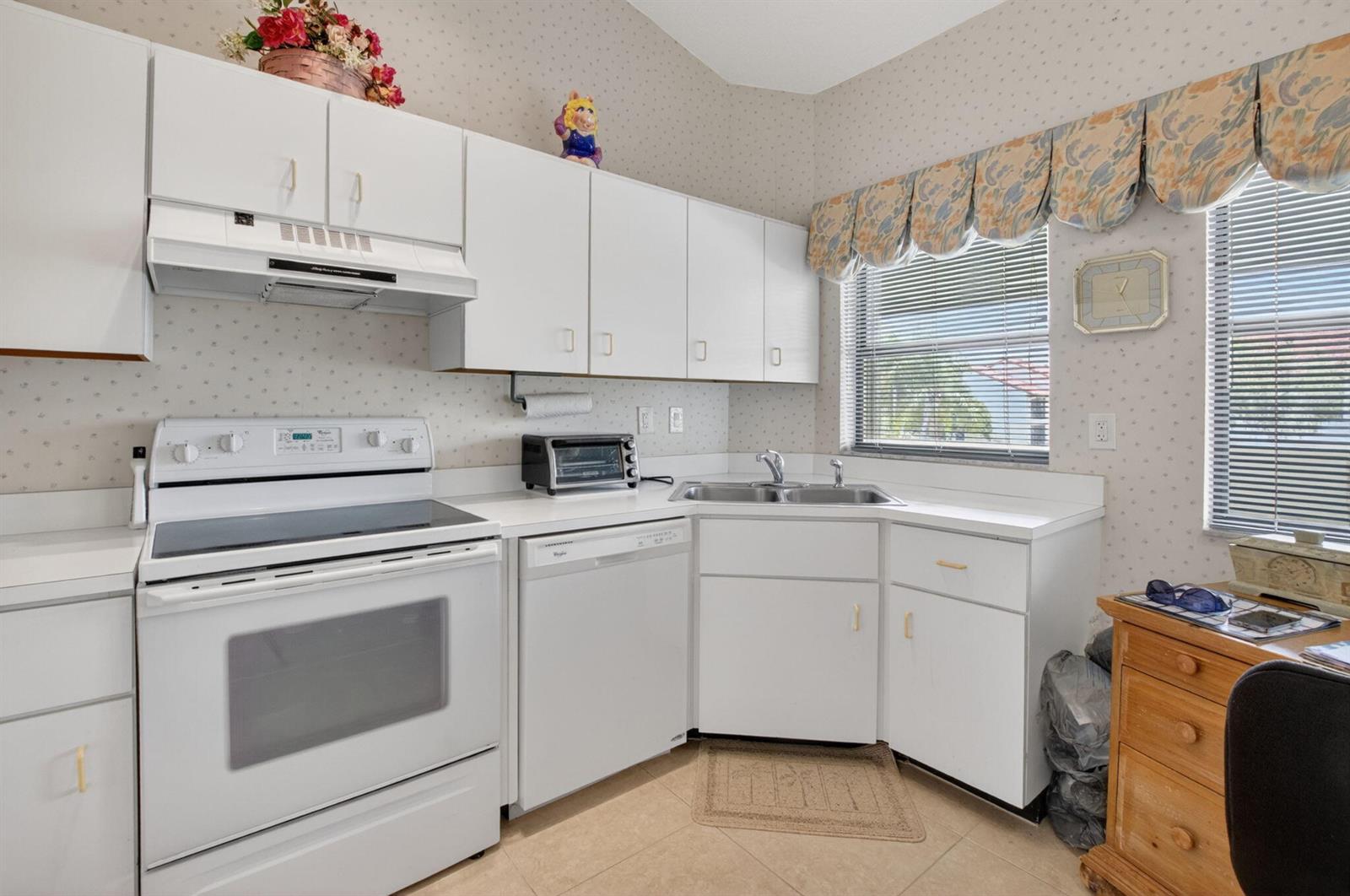 A kitchen with white cabinets, white appliances, patterned wallpaper, and a corner sink — 5907 Parkwalk Drive, Boynton Beach FL 33472, BOYNTON BEACH, FL