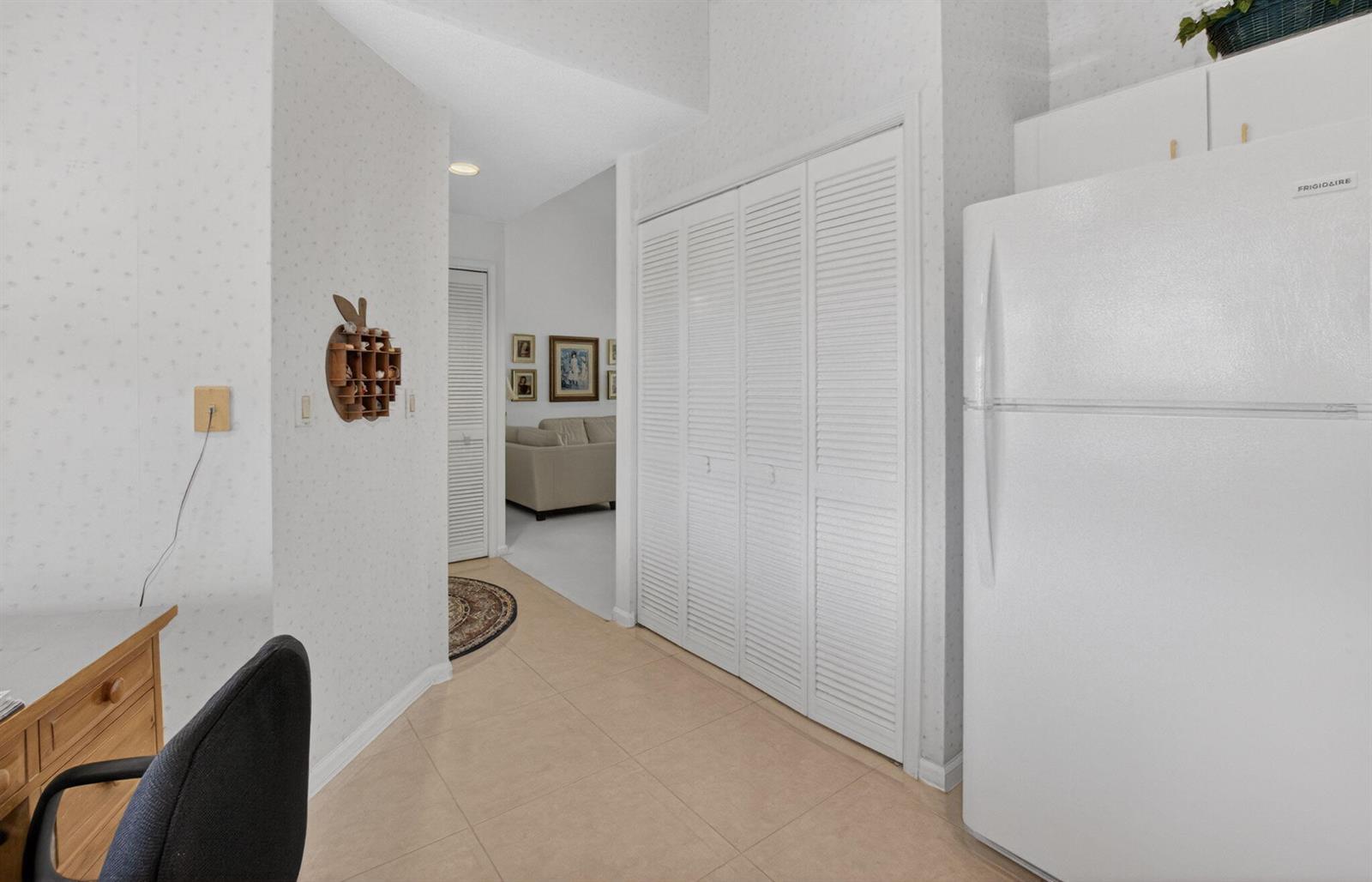 A kitchen area features a white refrigerator, louvered closet doors, and light-colored tile flooring — 5907 Parkwalk Drive, Boynton Beach FL 33472, BOYNTON BEACH, FL