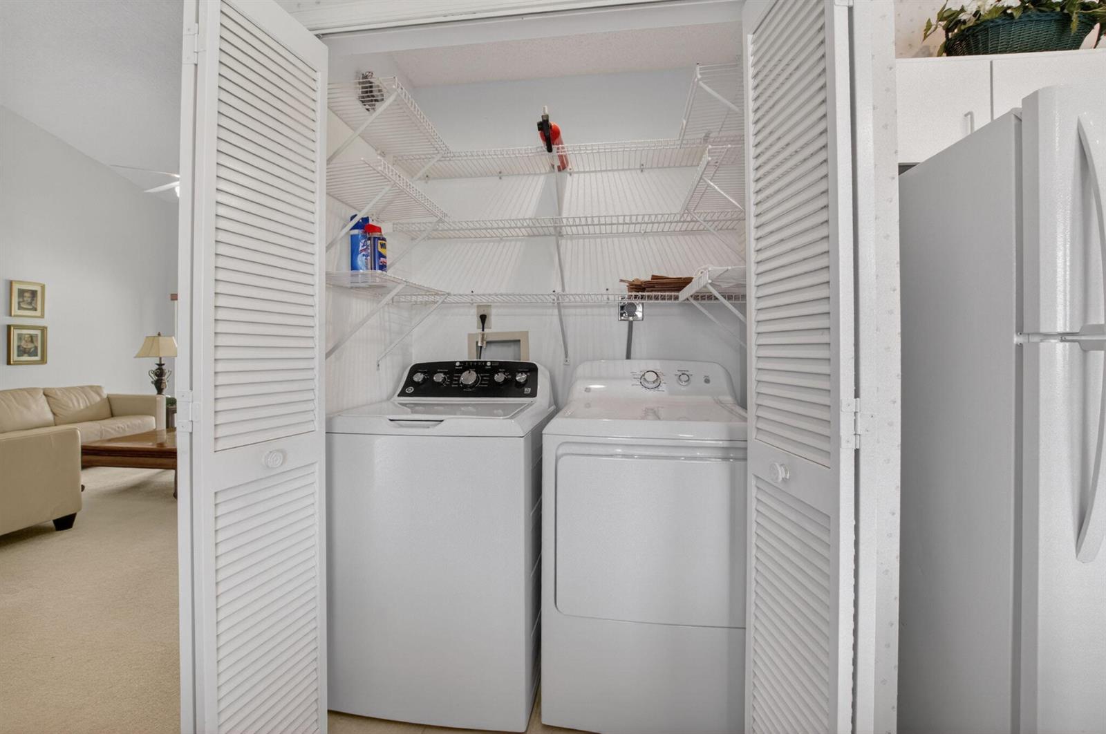 A laundry closet with white appliances and wire shelving sits next to a refrigerator — 5907 Parkwalk Drive, Boynton Beach FL 33472, BOYNTON BEACH, FL