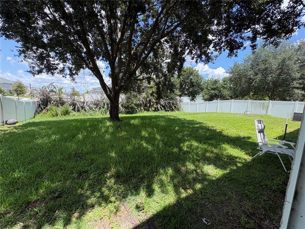 A grassy backyard features a large tree, a white vinyl fence, and a folding chair — 12332 BELCROFT DRIVE, RIVERVIEW, FL