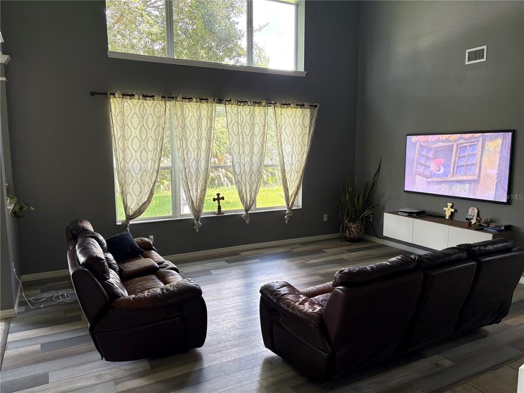 A living room features dark gray walls, wood-look flooring, two leather sofas, and large windows — 12332 BELCROFT DRIVE, RIVERVIEW, FL