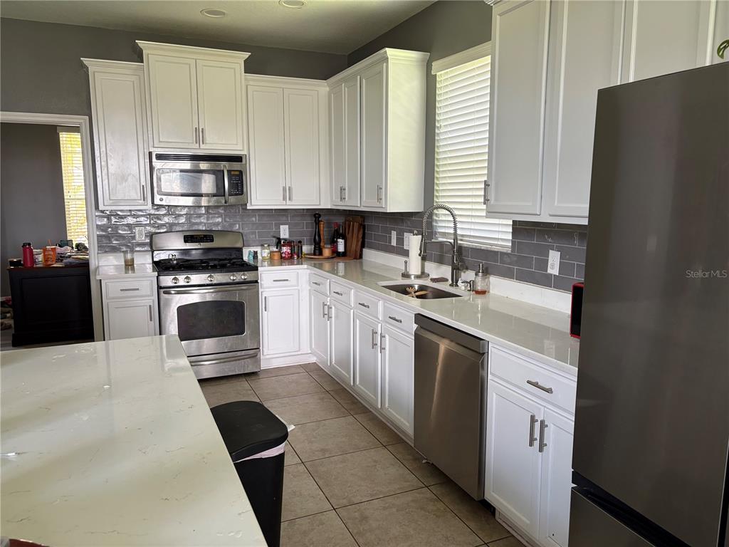 A kitchen features white cabinets, stainless steel appliances, a gray tile backsplash, and quartz countertops — 12332 BELCROFT DRIVE, RIVERVIEW, FL