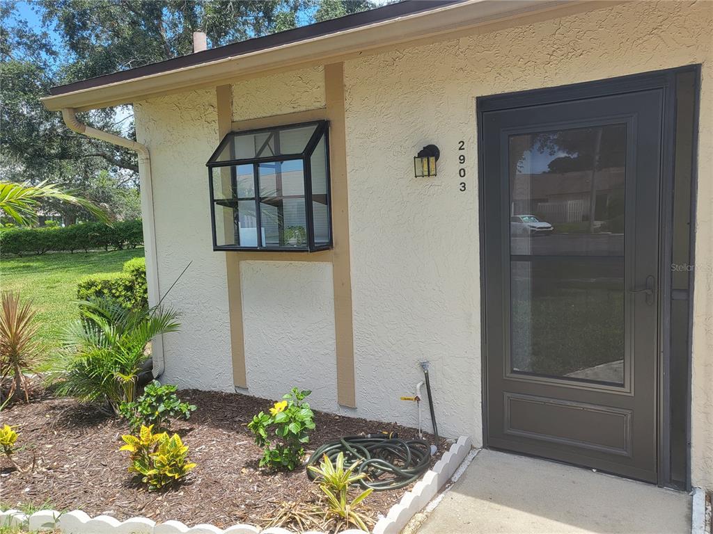 The exterior of a house features a greenhouse window, a dark storm door, and landscaping — 2903 63RD STREET W, BRADENTON, FL