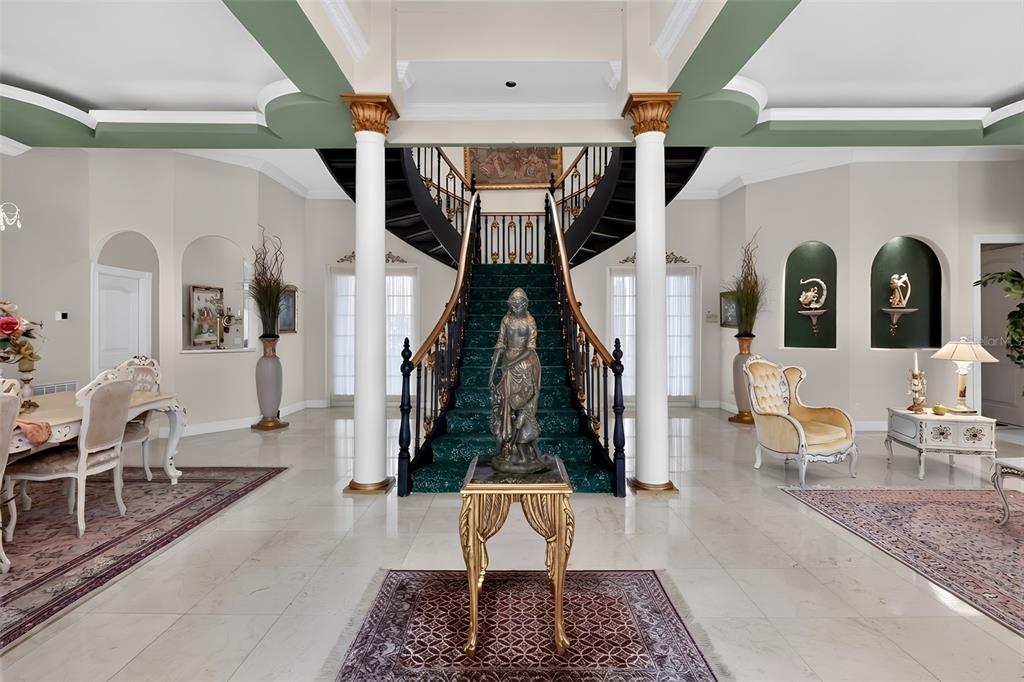 A grand foyer features a curved staircase, two white columns, and a central statue pedestal — 7957 S PARK PLACE, ORLANDO, FL