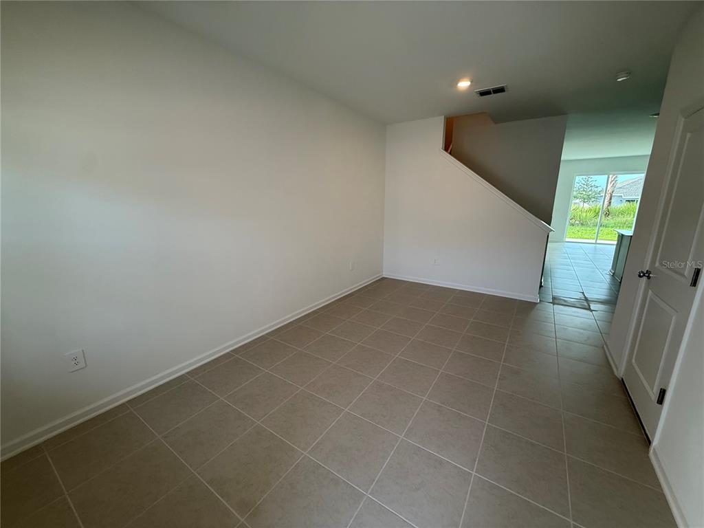 An empty room with beige tile flooring, white walls, and a staircase leading upstairs — 2567 SKYLIINE LOOP, KISSIMMEE, FL
