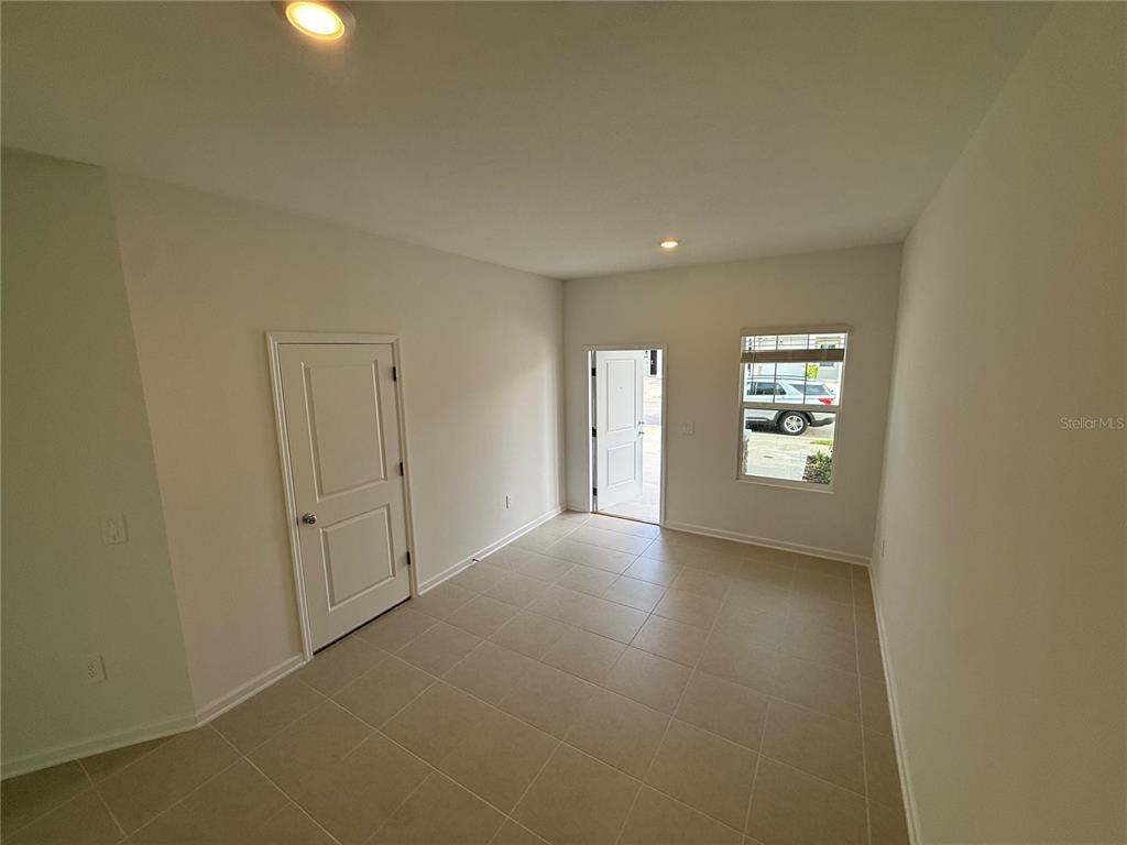 An empty room with light-colored tile flooring, white walls, a door, and a window — 2567 SKYLIINE LOOP, KISSIMMEE, FL