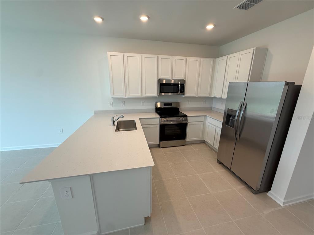 A kitchen features white cabinets, stainless steel appliances, a large island, and light-colored tile flooring — 2567 SKYLIINE LOOP, KISSIMMEE, FL
