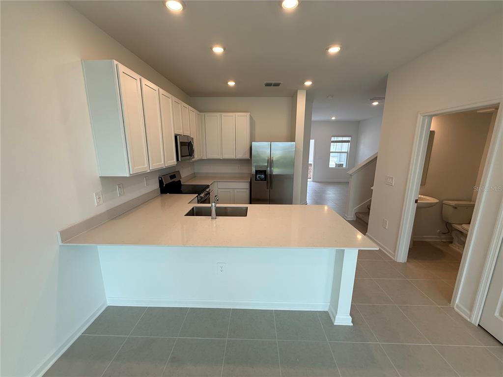 A kitchen with white cabinets, stainless steel appliances, and a peninsula countertop overlooks a hallway — 2567 SKYLIINE LOOP, KISSIMMEE, FL