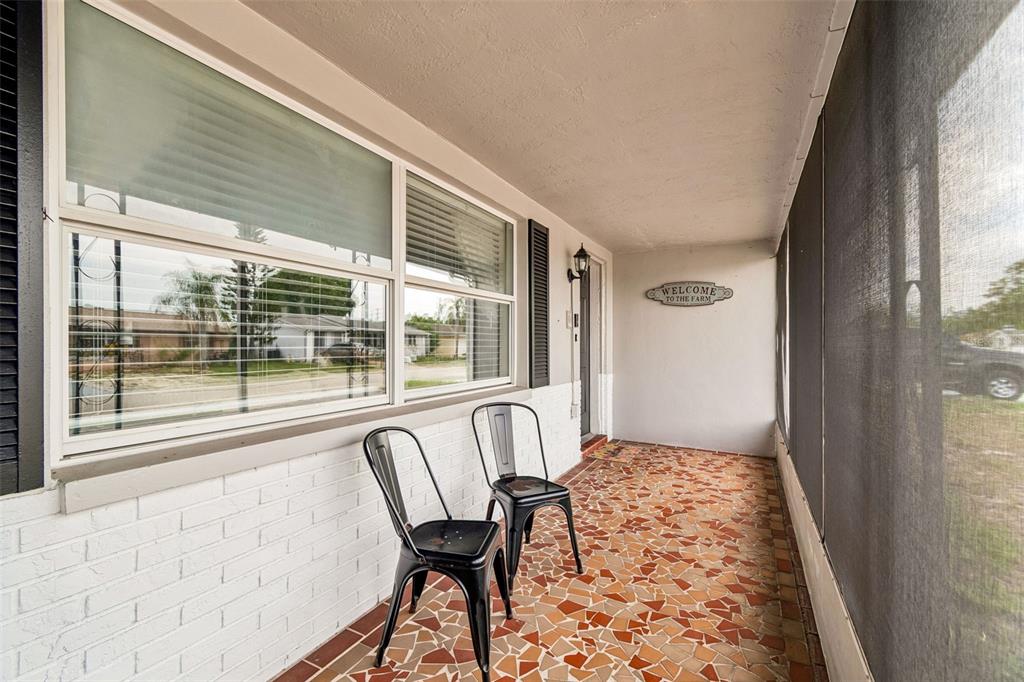 A covered porch features a mosaic tile floor, two black metal chairs, and white brick — 5915 OTIS DRIVE, NEW PORT RICHEY, FL