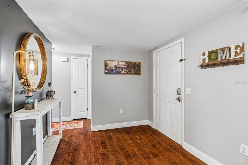 An entryway features wood-look flooring, a white console table, a round mirror, and a white door — 5915 OTIS DRIVE, NEW PORT RICHEY, FL