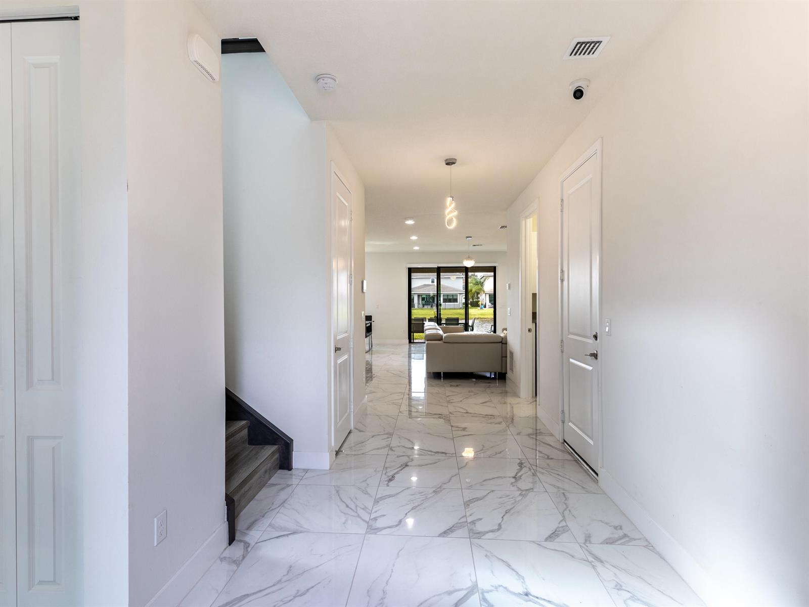 A bright hallway with white marble tile floors leads toward a living area with patio doors — 7191 Montereal Path, Lake Worth FL 33463, LAKE WORTH, FL
