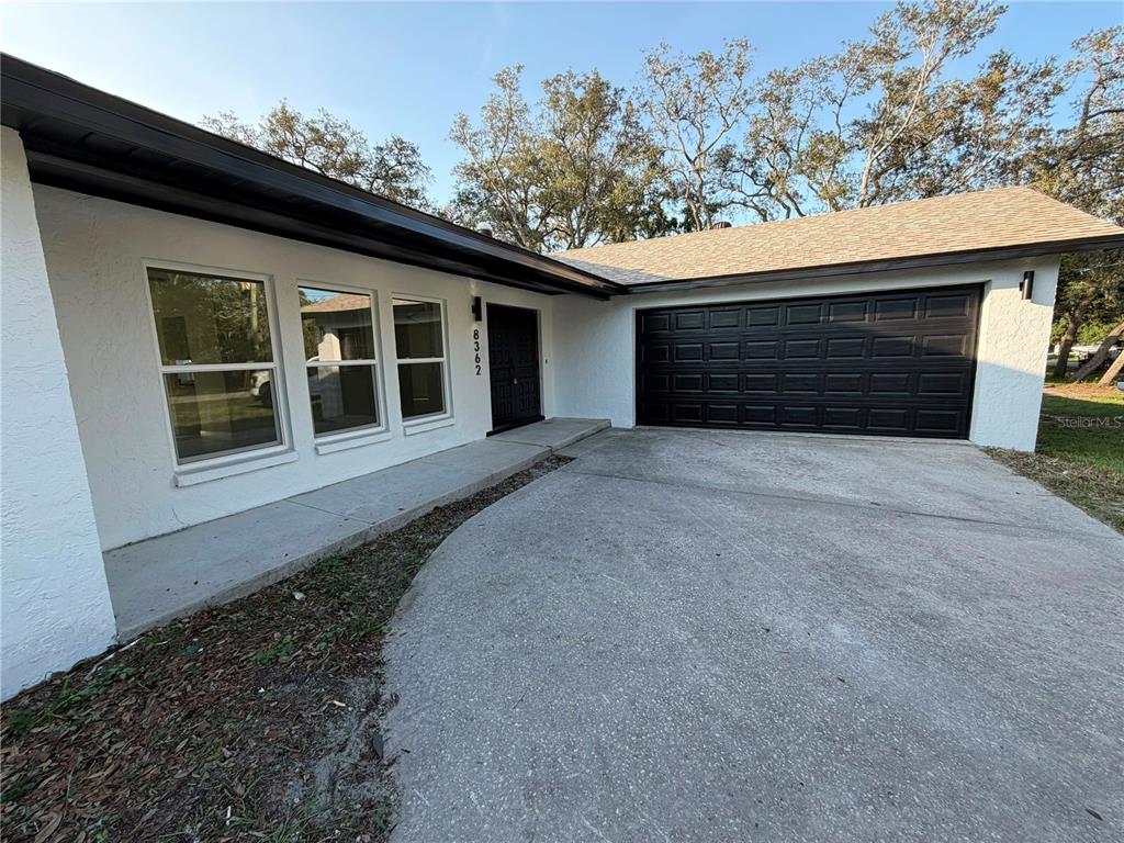 A white house exterior features a black garage door, a dark front door, and windows — 8362 TRANQUIL DRIVE, SPRING HILL, FL