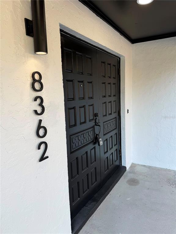 A black double door with a lockbox is set into a white stucco exterior wall — 8362 TRANQUIL DRIVE, SPRING HILL, FL