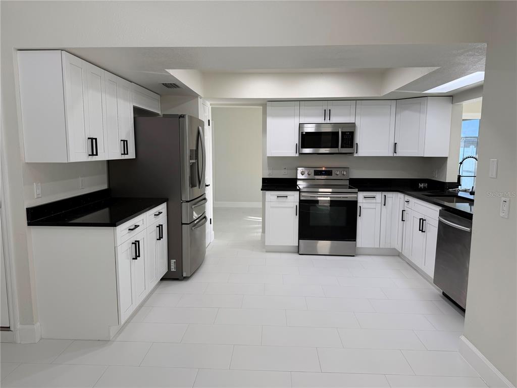 A kitchen features white cabinets, black countertops, stainless steel appliances, and white tile flooring — 8362 TRANQUIL DRIVE, SPRING HILL, FL