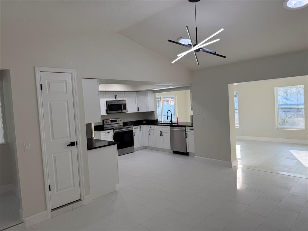 A kitchen with white cabinets, black countertops, stainless steel appliances, and a modern light fixture — 8362 TRANQUIL DRIVE, SPRING HILL, FL
