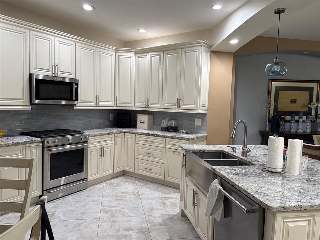 A kitchen features cream-colored cabinets, granite countertops, stainless steel appliances, and a farmhouse sink — 30335 LETTINGWELL CIRCLE, WESLEY CHAPEL, FL