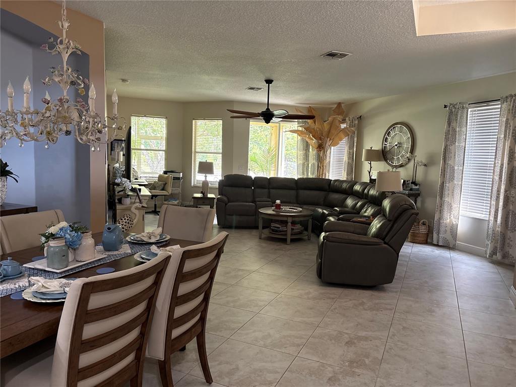 An open-concept living and dining area features tile flooring, a sectional sofa, and a chandelier — 30335 LETTINGWELL CIRCLE, WESLEY CHAPEL, FL