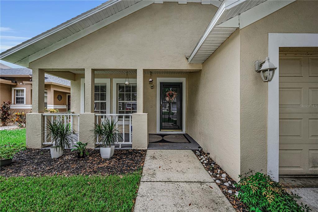 A beige house exterior features a covered front porch, a concrete walkway, and a garage — 5229 MANGO FRUIT STREET, SEFFNER, FL