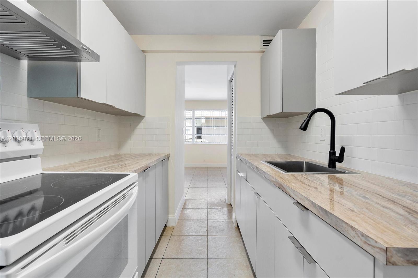 A galley kitchen features light gray cabinets, wood-look countertops, and a black faucet — 1715 N 16th Ave # 102, Hollywood FL 33020, HOLLYWOOD, FL