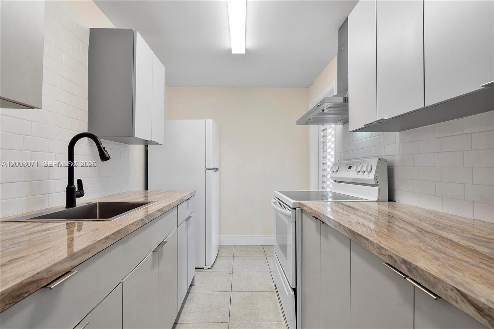 A galley kitchen features light gray cabinets, wood-look countertops, white subway tile, and white appliances — 1715 N 16th Ave # 102, Hollywood FL 33020, HOLLYWOOD, FL