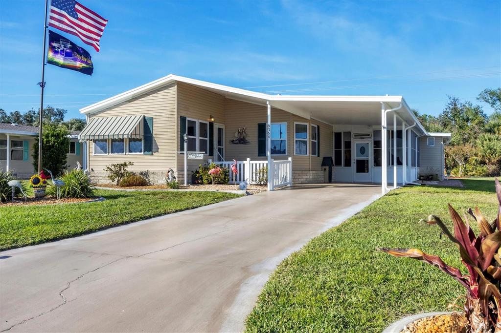 A tan manufactured home with a concrete driveway, carport, and an American flag — 8364 KINGLET DRIVE, ENGLEWOOD, FL