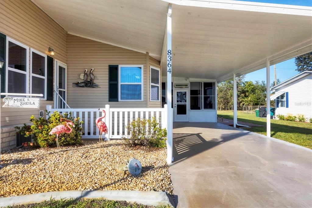 The exterior of a manufactured home features a carport, a white fence, and landscaping — 8364 KINGLET DRIVE, ENGLEWOOD, FL