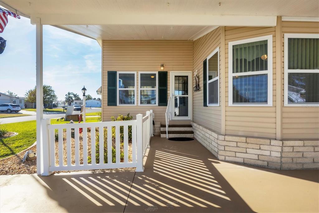 A tan mobile home features a covered concrete porch with a white vinyl railing — 8364 KINGLET DRIVE, ENGLEWOOD, FL