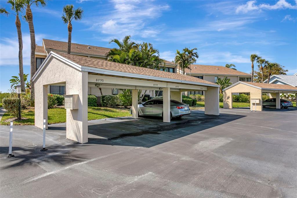 A covered parking structure with numbered spaces sits in front of a multi-story apartment building — 8734 54TH AVENUE W UNIT 8734, BRADENTON, FL