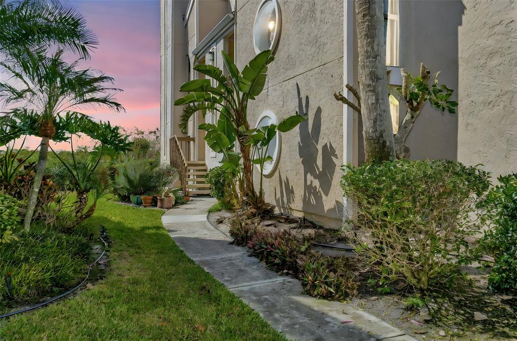 A concrete walkway leads past tropical landscaping and a building exterior with two round windows — 8734 54TH AVENUE W UNIT 8734, BRADENTON, FL