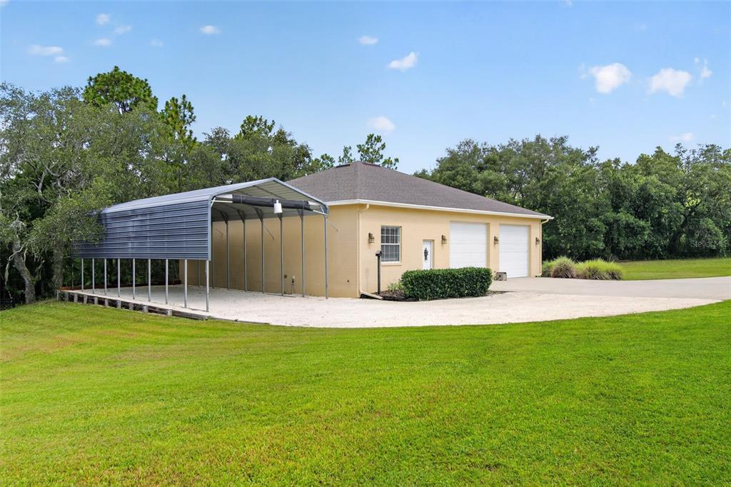 A detached garage with a metal carport extension sits on a grassy lot with trees — 4348 W BONANZA DRIVE, BEVERLY HILLS, FL