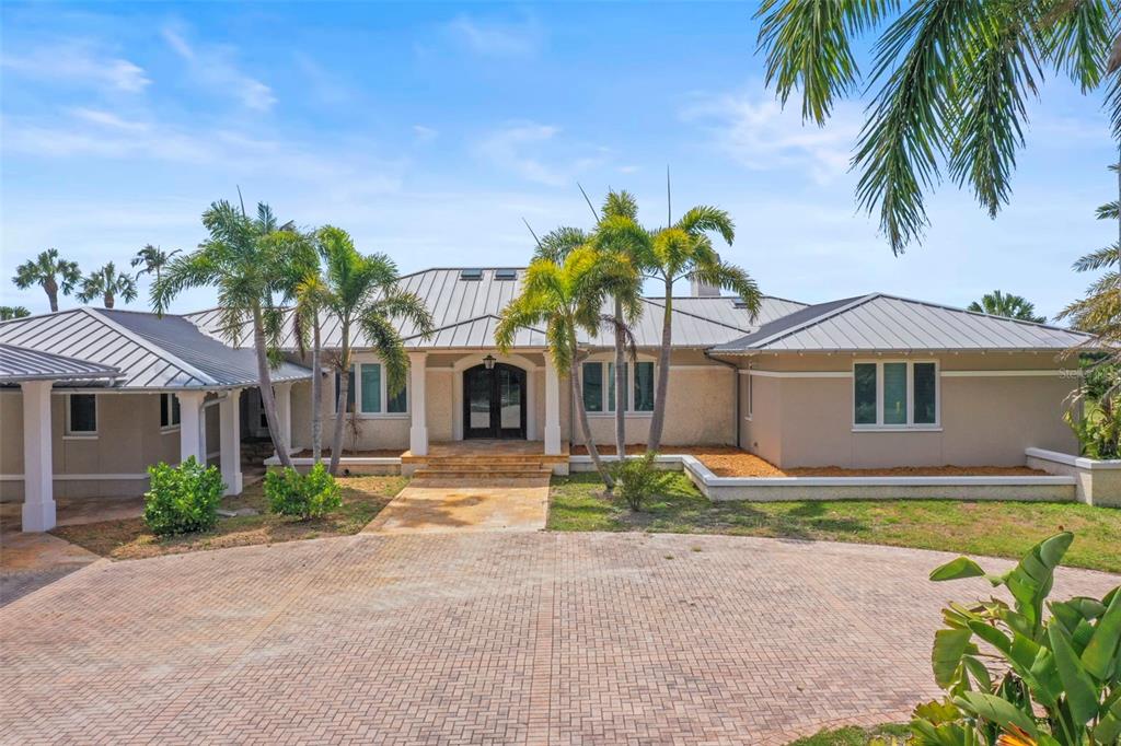 A single-story house with a metal roof, beige stucco walls, and a brick paver driveway — 1721 GULF ROAD, TARPON SPRINGS, FL