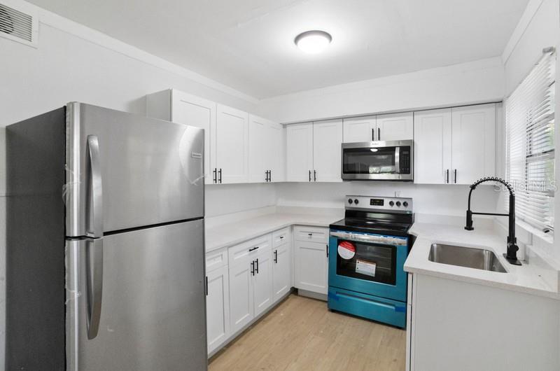 A kitchen features white cabinets, stainless steel appliances, and light-colored wood flooring — 2608 E CAYUGA STREET, TAMPA, FL