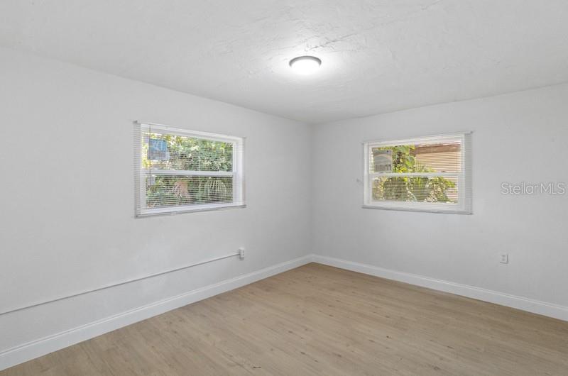 An empty bedroom features white walls, light wood-look flooring, and two windows with blinds — 2608 E CAYUGA STREET, TAMPA, FL