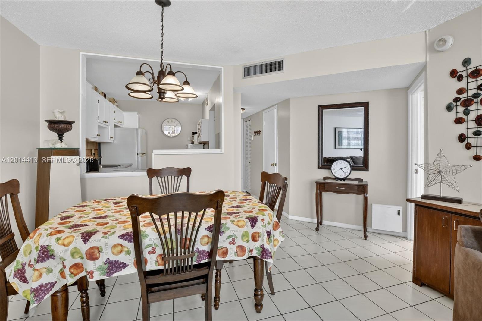 A dining area features a fruit-patterned tablecloth, wooden chairs, tile flooring, and a kitchen pass-through — 1817 S Ocean Dr # 225, Hallandale Beach FL 33009, HALLANDALE BEACH, FL