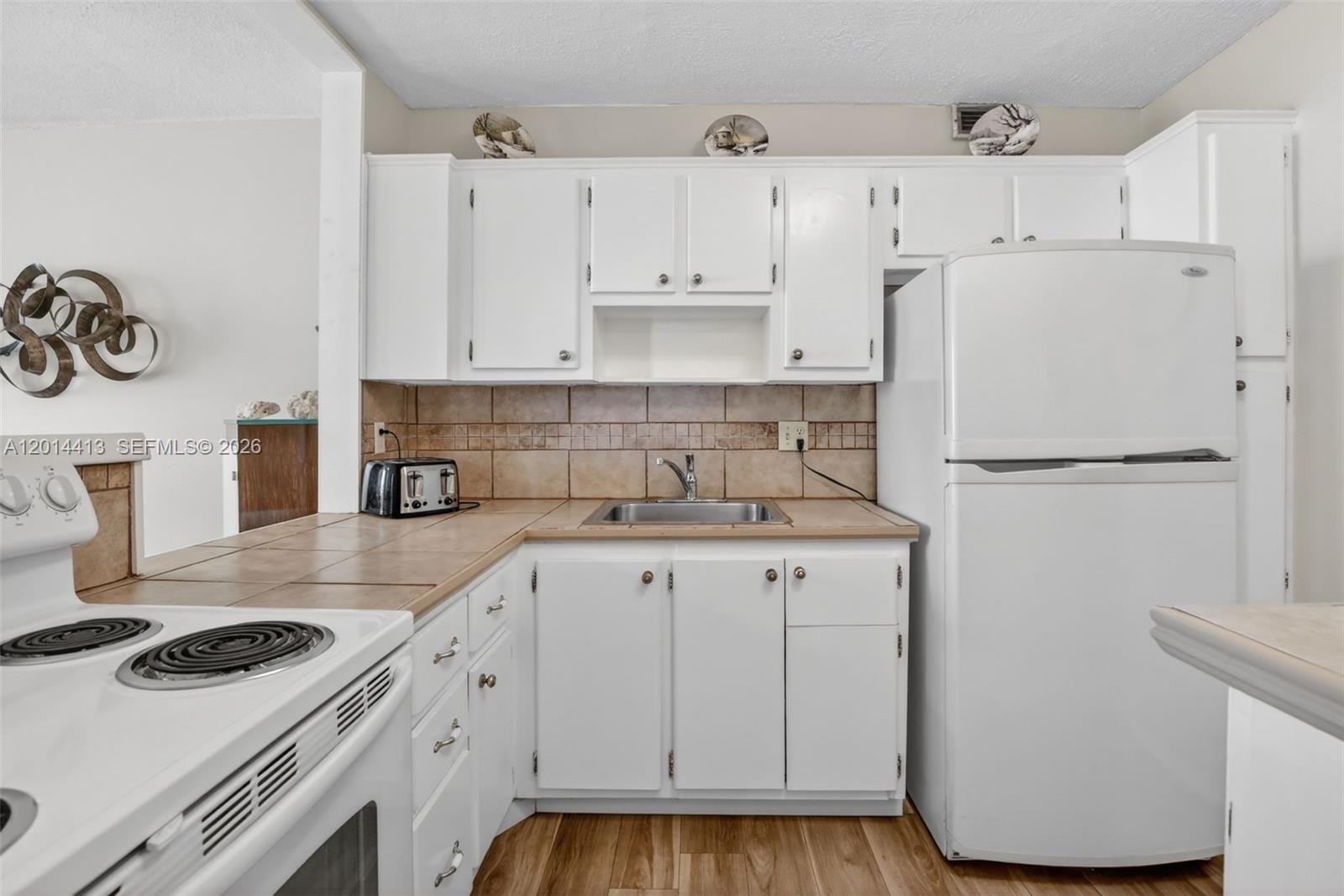 A kitchen features white cabinets, tile countertops, a stainless steel sink, and white appliances — 1817 S Ocean Dr # 225, Hallandale Beach FL 33009, HALLANDALE BEACH, FL