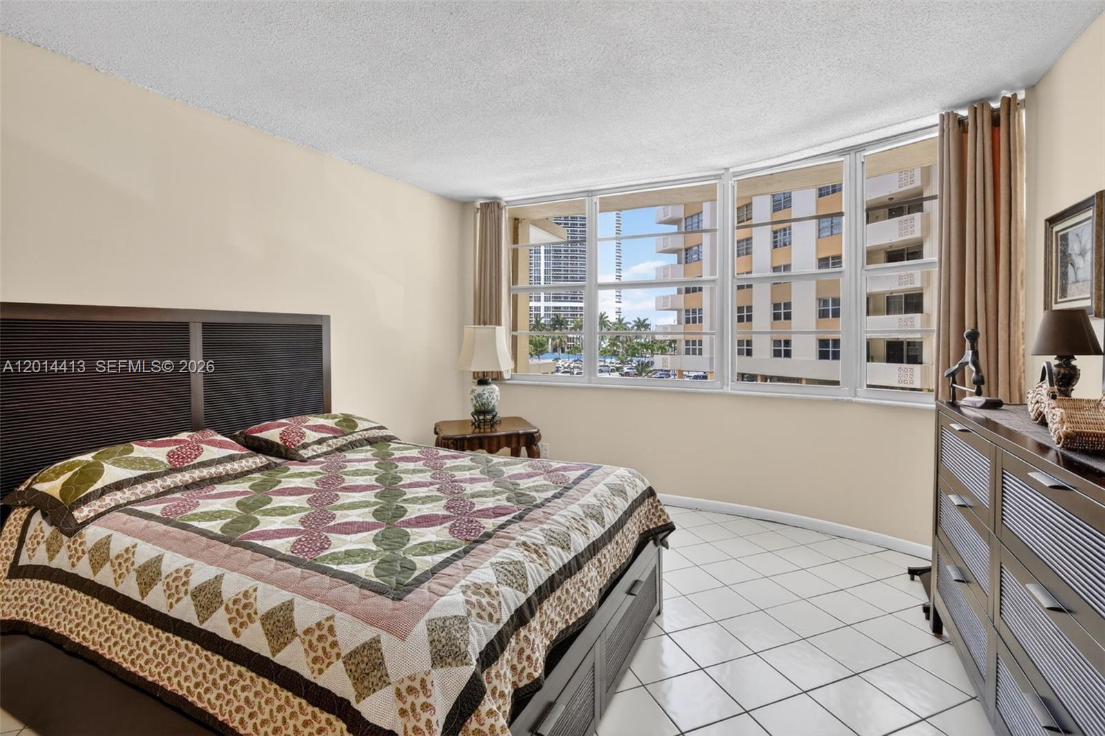 A bedroom features a patterned quilt on the bed, tiled floors, and large windows — 1817 S Ocean Dr # 225, Hallandale Beach FL 33009, HALLANDALE BEACH, FL