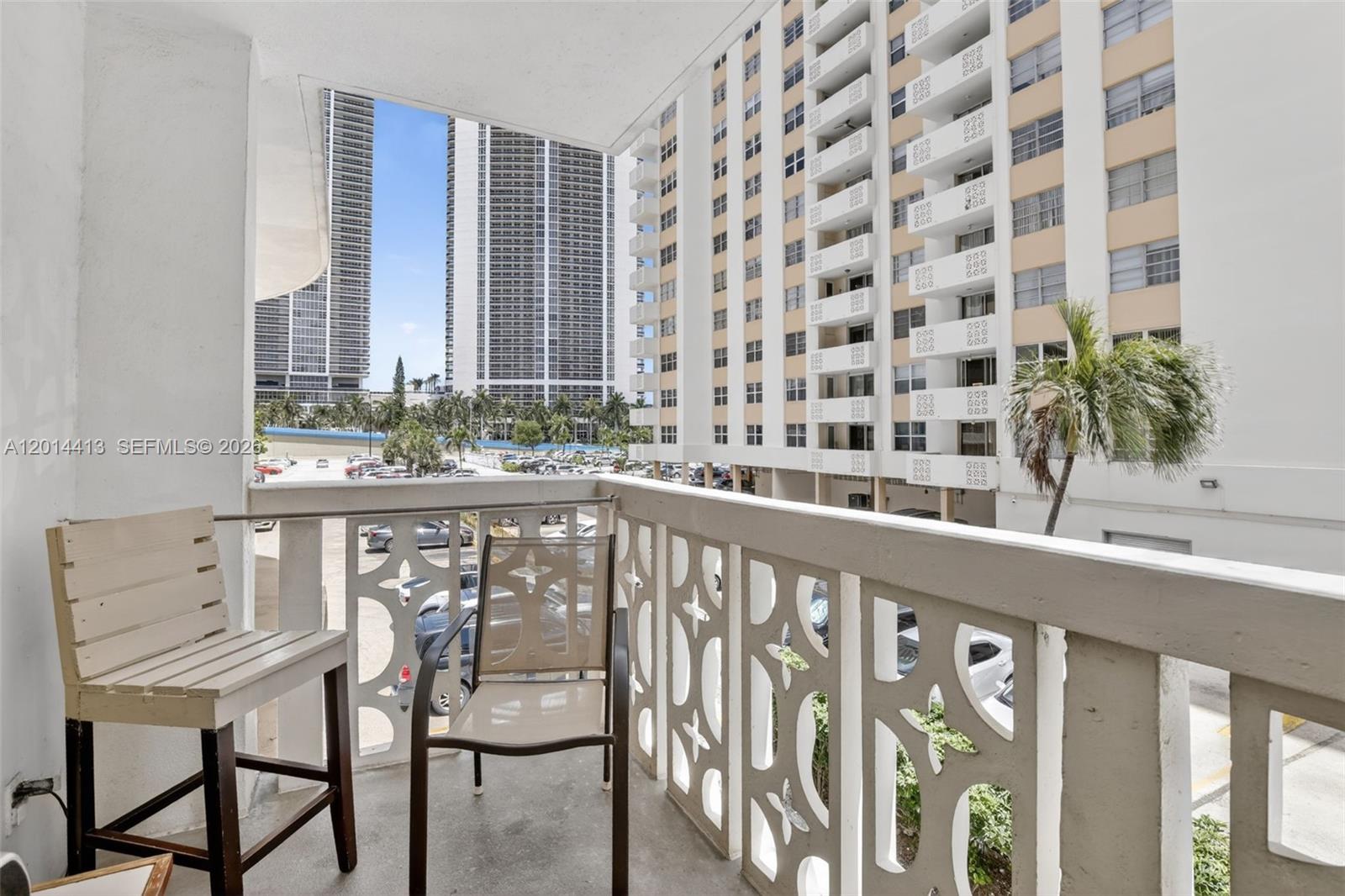 A balcony features a decorative white railing, two chairs, and a view of nearby buildings — 1817 S Ocean Dr # 225, Hallandale Beach FL 33009, HALLANDALE BEACH, FL