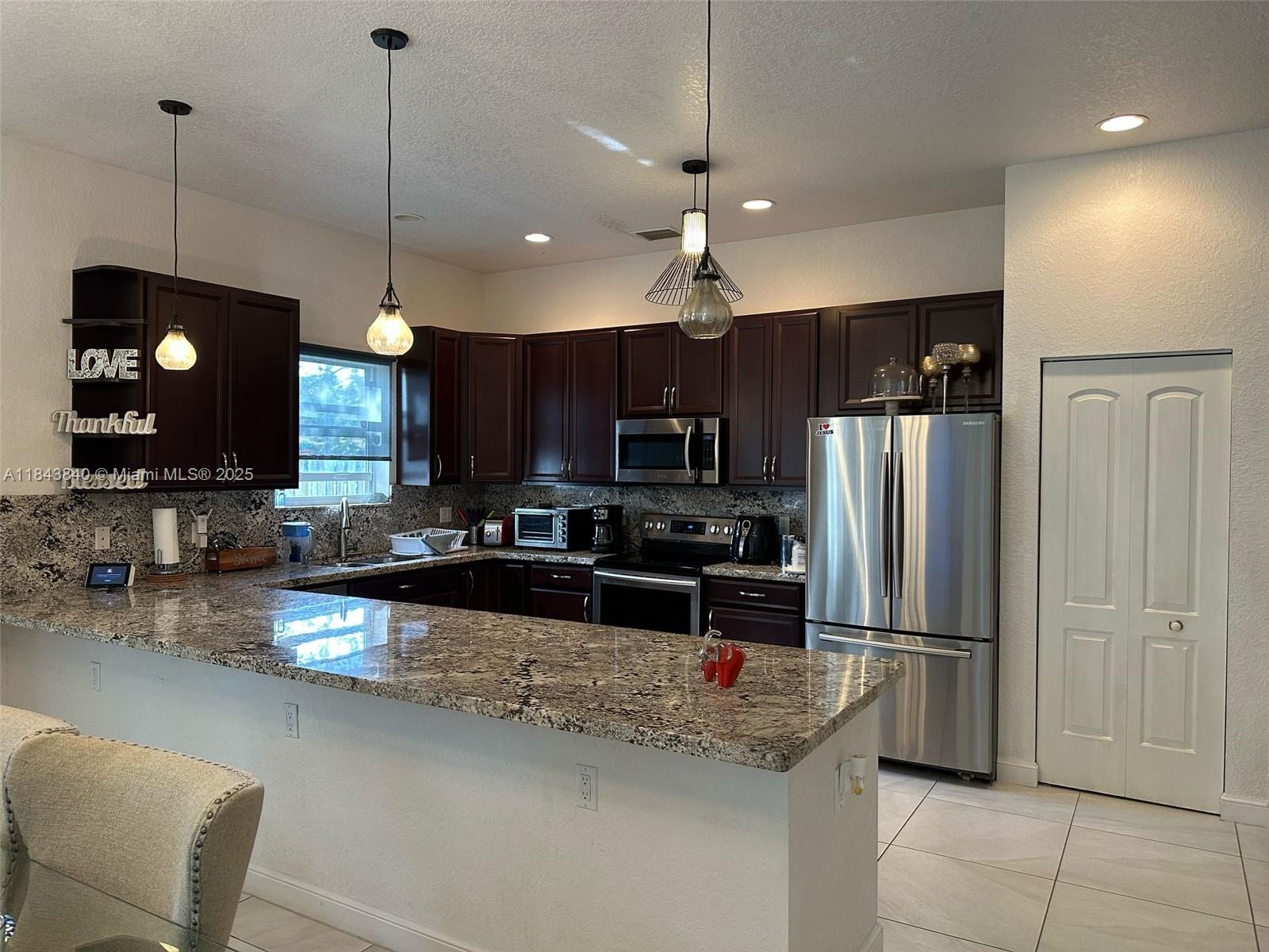 A kitchen features dark wood cabinets, granite countertops, stainless steel appliances, and two pendant lights — 210 SW 4th St # 210, Dania Beach FL 33004, DANIA BEACH, FL
