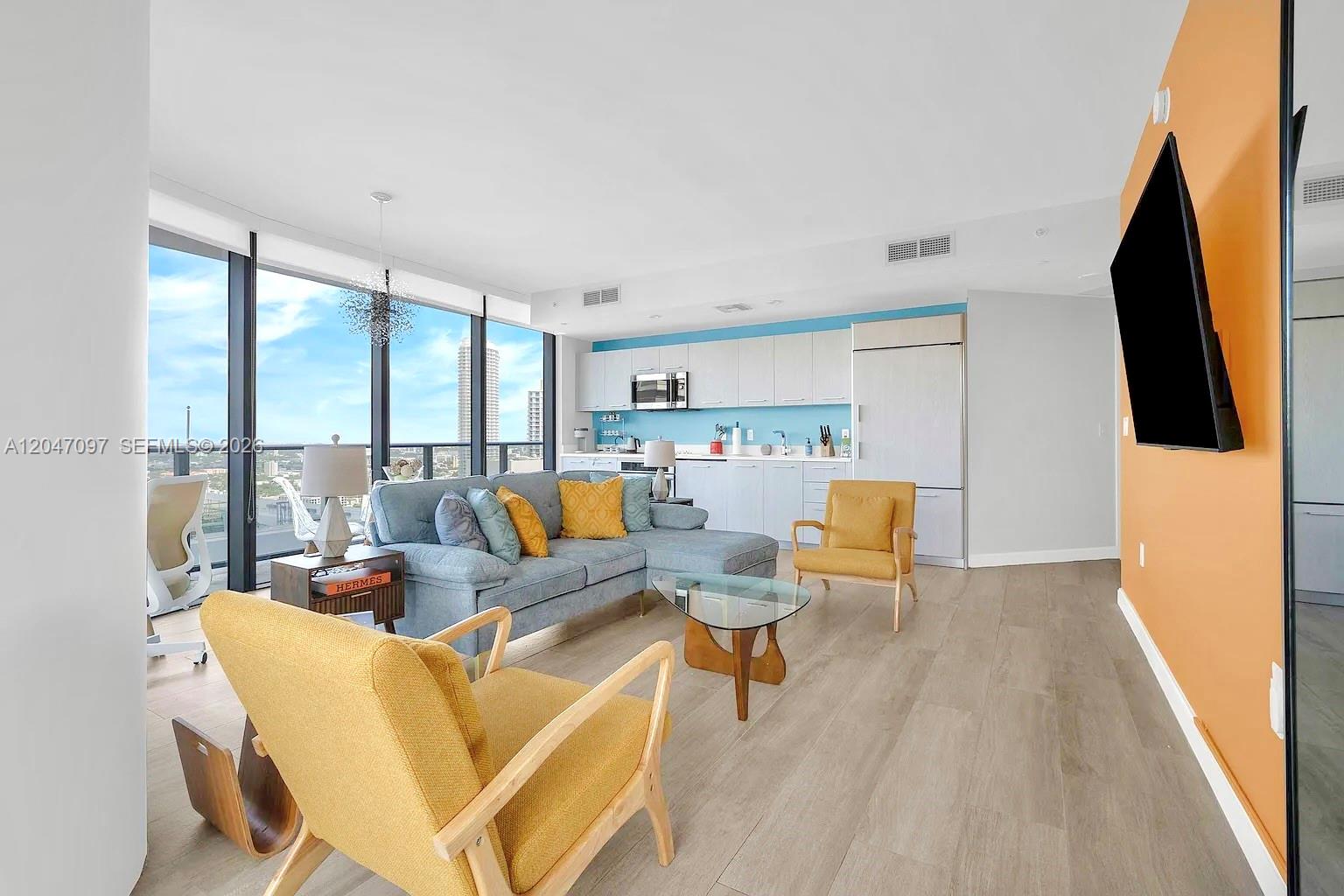 A living room with a blue sofa, yellow armchairs, and a kitchen against a blue wall — 55 SW 9th St # 3306, Miami FL 33130, MIAMI, FL