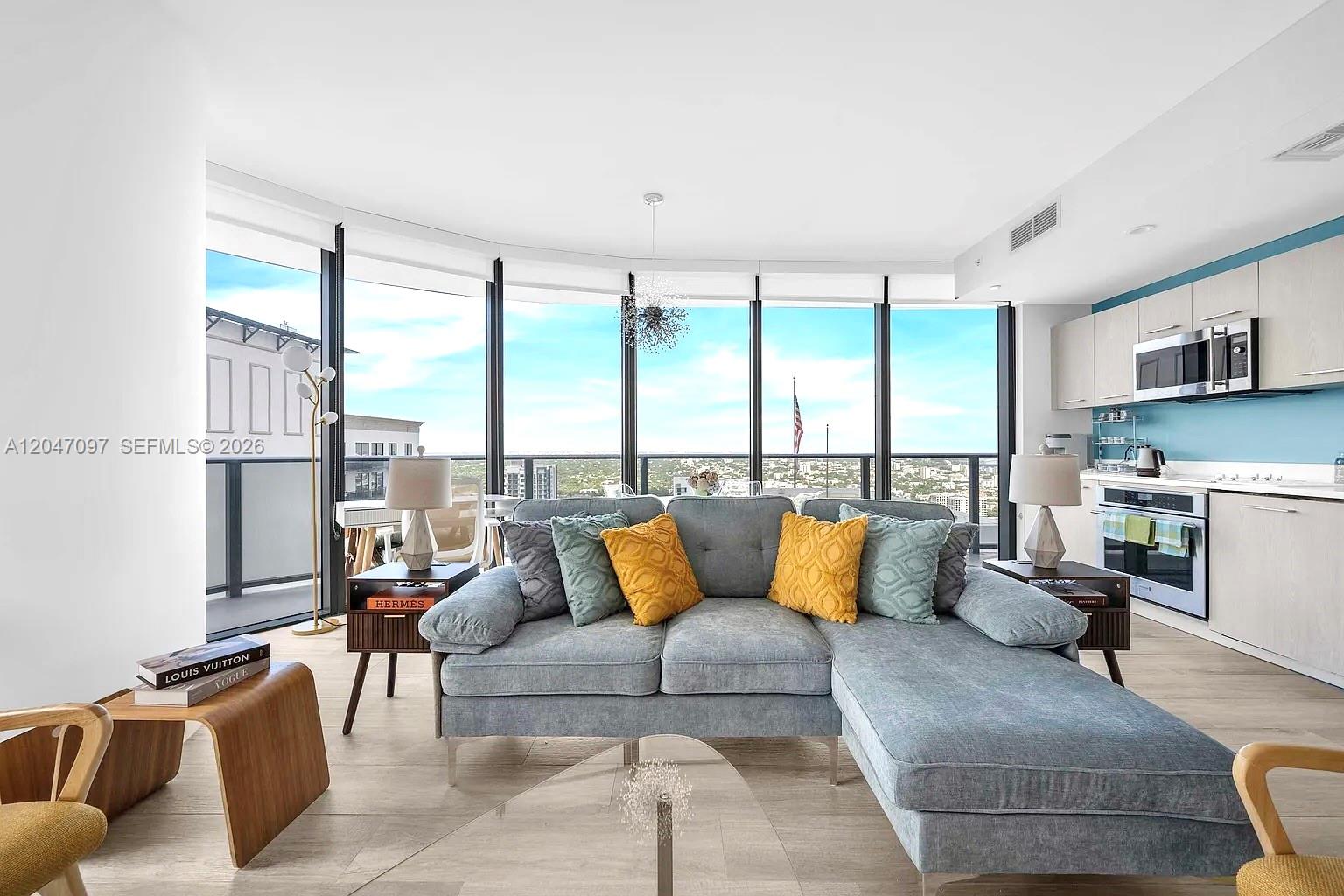 A modern living room features a gray sectional sofa, floor-to-ceiling windows, and an open kitchen — 55 SW 9th St # 3306, Miami FL 33130, MIAMI, FL