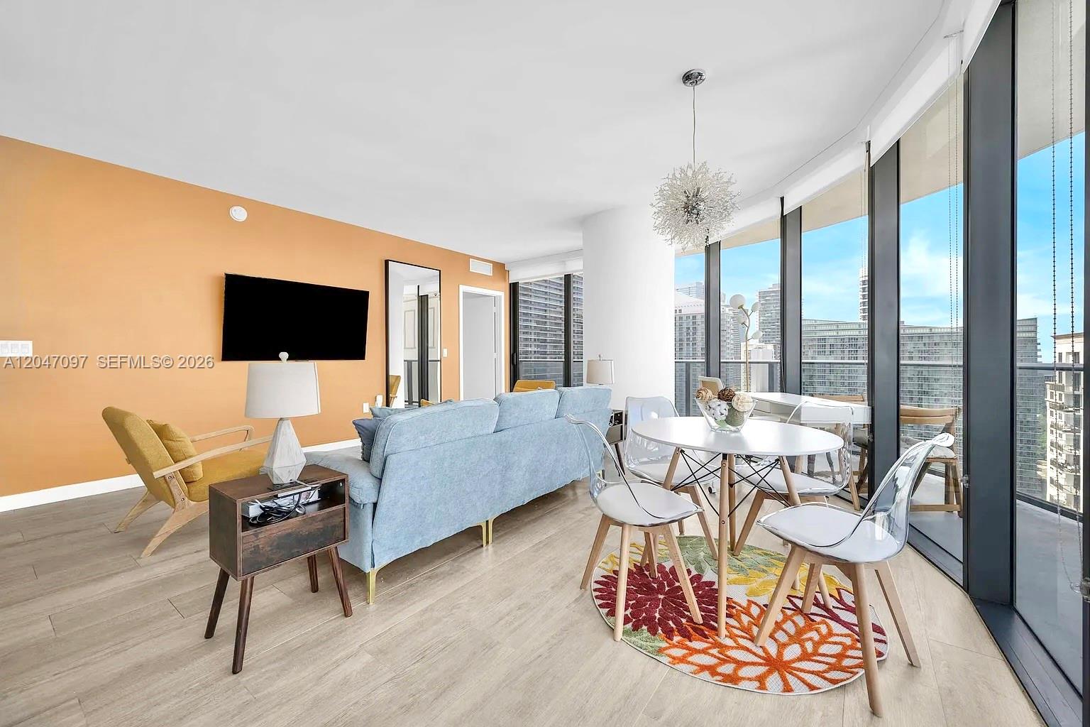 A living and dining area features an orange accent wall, light wood floors, and floor-to-ceiling windows — 55 SW 9th St # 3306, Miami FL 33130, MIAMI, FL