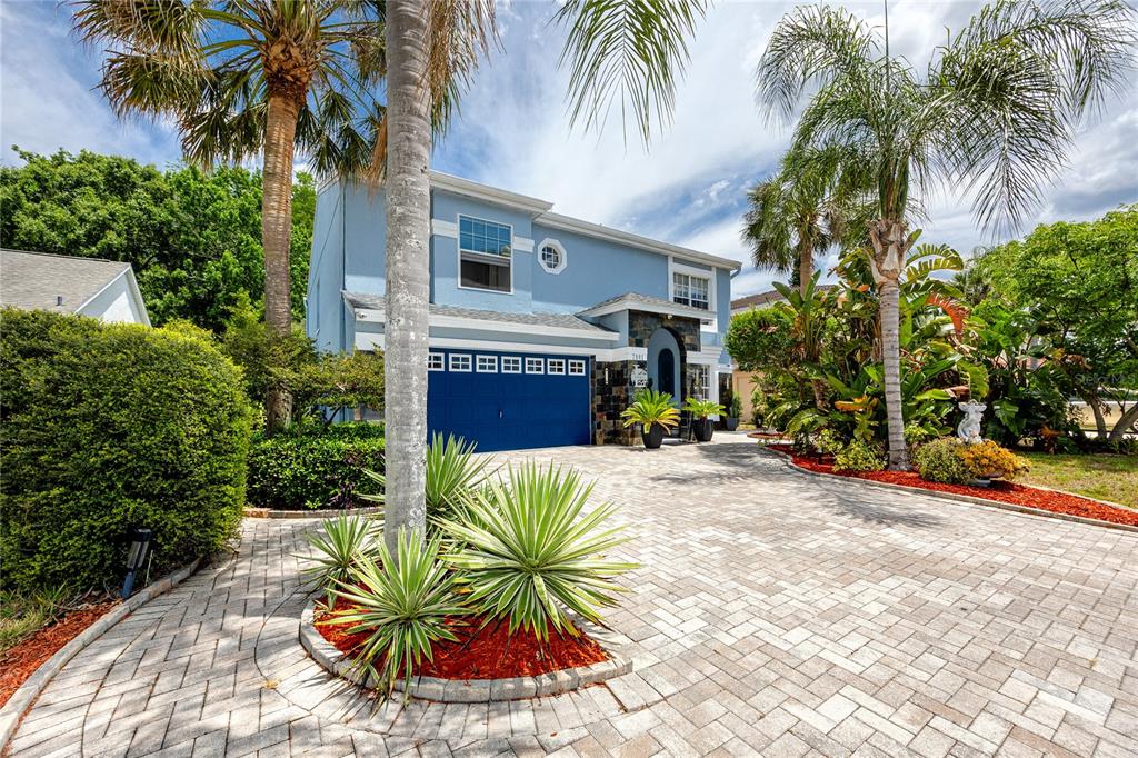 A two-story blue house features a paved driveway, a garage, and tropical landscaping — 7801 HAMLET DRIVE, NEW PORT RICHEY, FL
