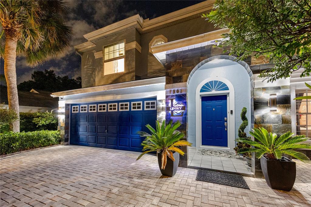 A two-story house exterior features a blue garage door, a blue front door, and stone accents — 7801 HAMLET DRIVE, NEW PORT RICHEY, FL